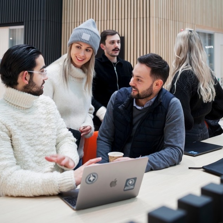 A group of students chatting in front of a laptop.