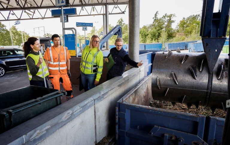 Fyra personer tittar ner i en stor återvinningscontainer på en återvinningscentral